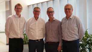 Four business men posing for an official photo in an office